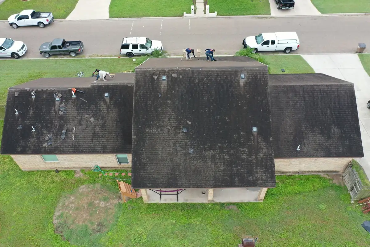 Crew removing badly weathered shingles during a full roof replacement in the Rio Grande Valley